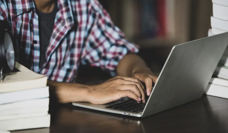 Une personne travaille sur un ordinateur portable, des livres à ses côtés.